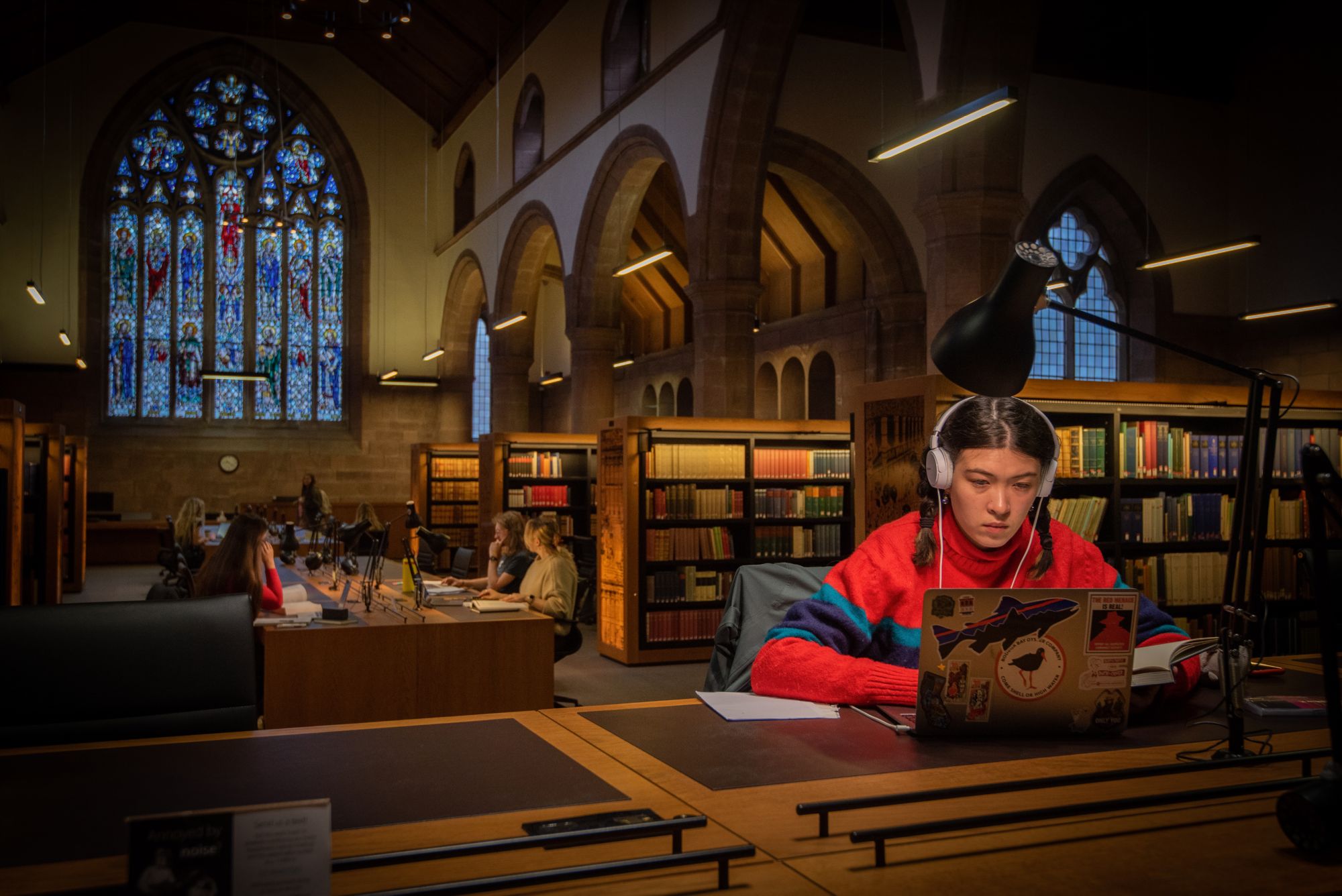 A student wearing headphones working on their laptop in the library